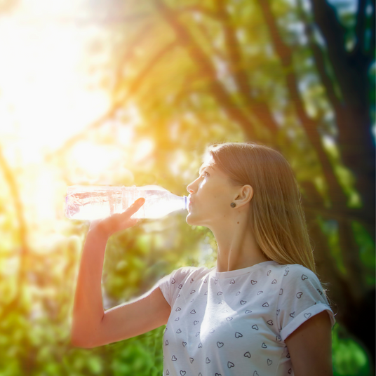 Woman drinking from a water bottle in a sunlit outdoor setting.