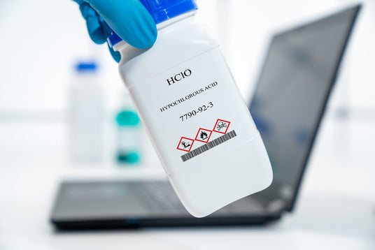 Bottle of hypochlorous acid with safety hazard symbols, held by a person wearing a blue glove.