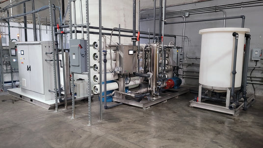Industrial equipment setup featuring pipes, tanks, and a control panel in a factory environment.