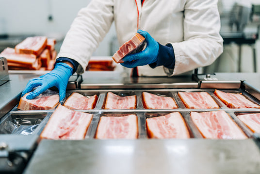 Worker in gloves handling slices of meat in a food processing facility.