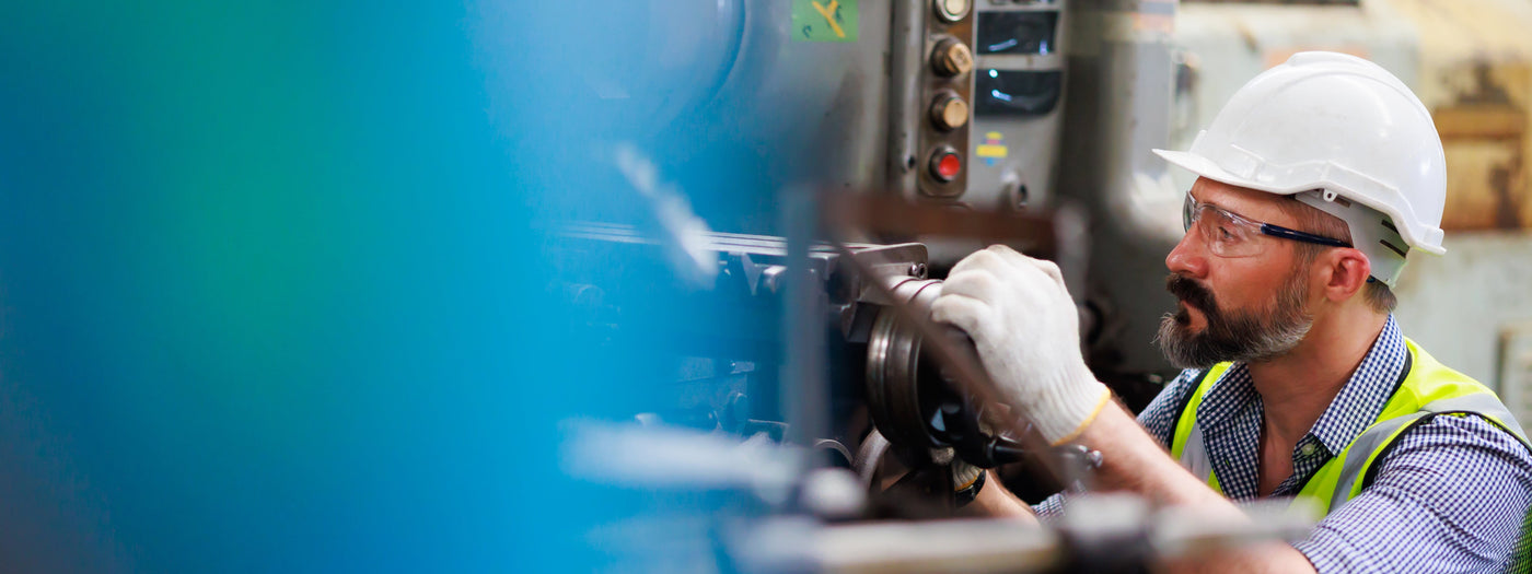 Worker in safety gear operating machinery in an industrial setting.