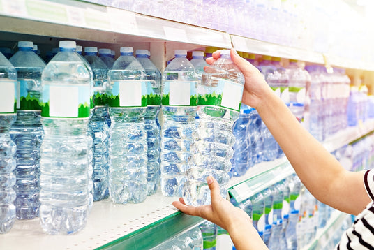 Person selecting a plastic water bottle from a store shelf filled with bottled water.