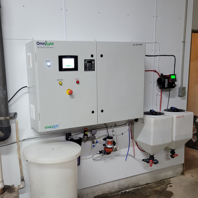 OmniLyte control panel with touchscreen display and adjacent solution tanks in an industrial setting.