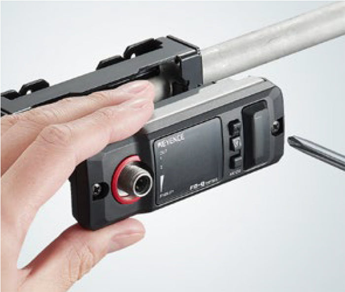 A hand adjusting a KEYENCE device attached to a metal rod, with tools nearby.