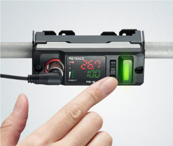 Digital display device mounted on a pipe, with a finger interacting with the buttons and an illuminated green light.