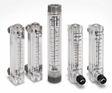 Five clear plastic flow meters with black measurement markings and black fittings, arranged on a light gray studio background. The set includes different flow meter models, with one central taller meter and four shorter side meters.