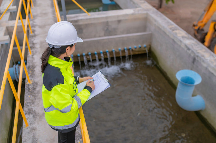 Woman in safety gear observing water treatment facility, taking notes.