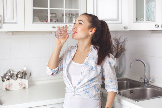 Woman drinking water in a kitchen setting.