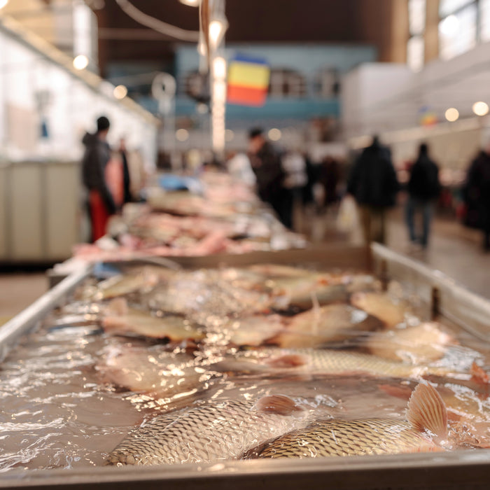 Fish displayed on tables in a market, with customers browsing in the background.