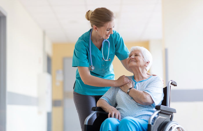 Nurse comforting elderly woman in wheelchair in a hospital hallway.