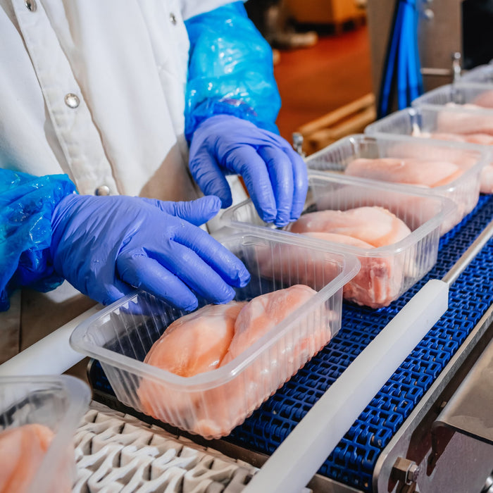Worker packaging fresh chicken fillets in plastic trays on a production line.