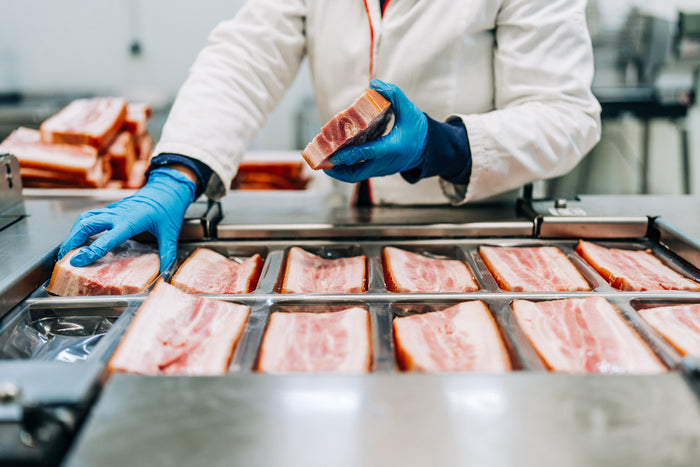 Worker in gloves handling slices of meat in a food processing facility.