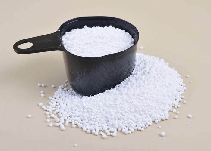 A black measuring cup filled with white granules, with some granules spilled on a light surface.