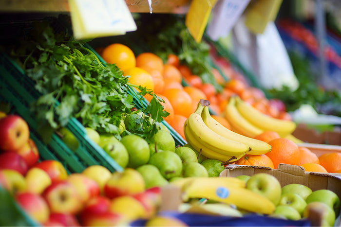 A colorful display of fresh fruits including apples, bananas, oranges, and greens at a market.