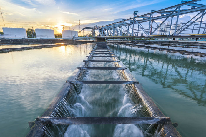 Water treatment facility with water flowing under a walkway at sunset.