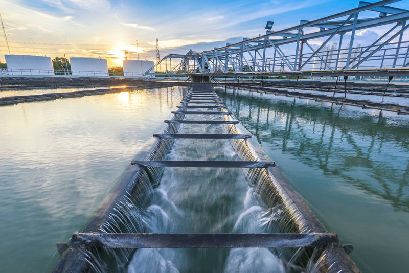 Water treatment facility with water flowing under a walkway at sunset.